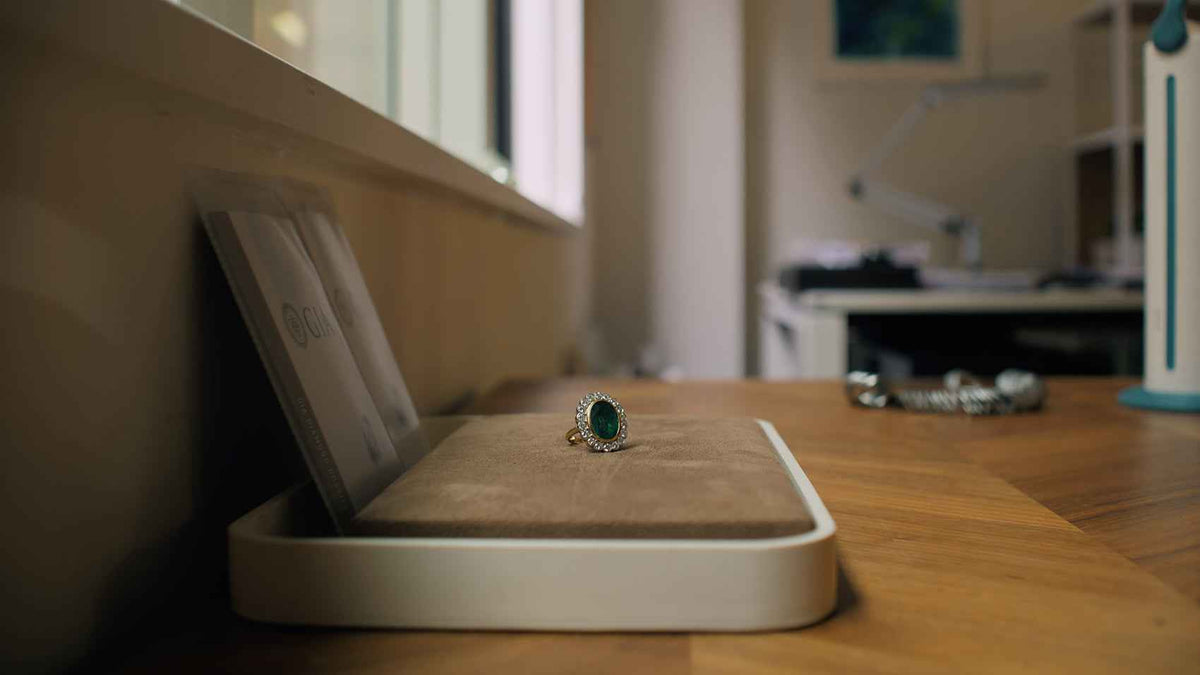 Emerald and diamond ring on a valuation tray in a bright office
