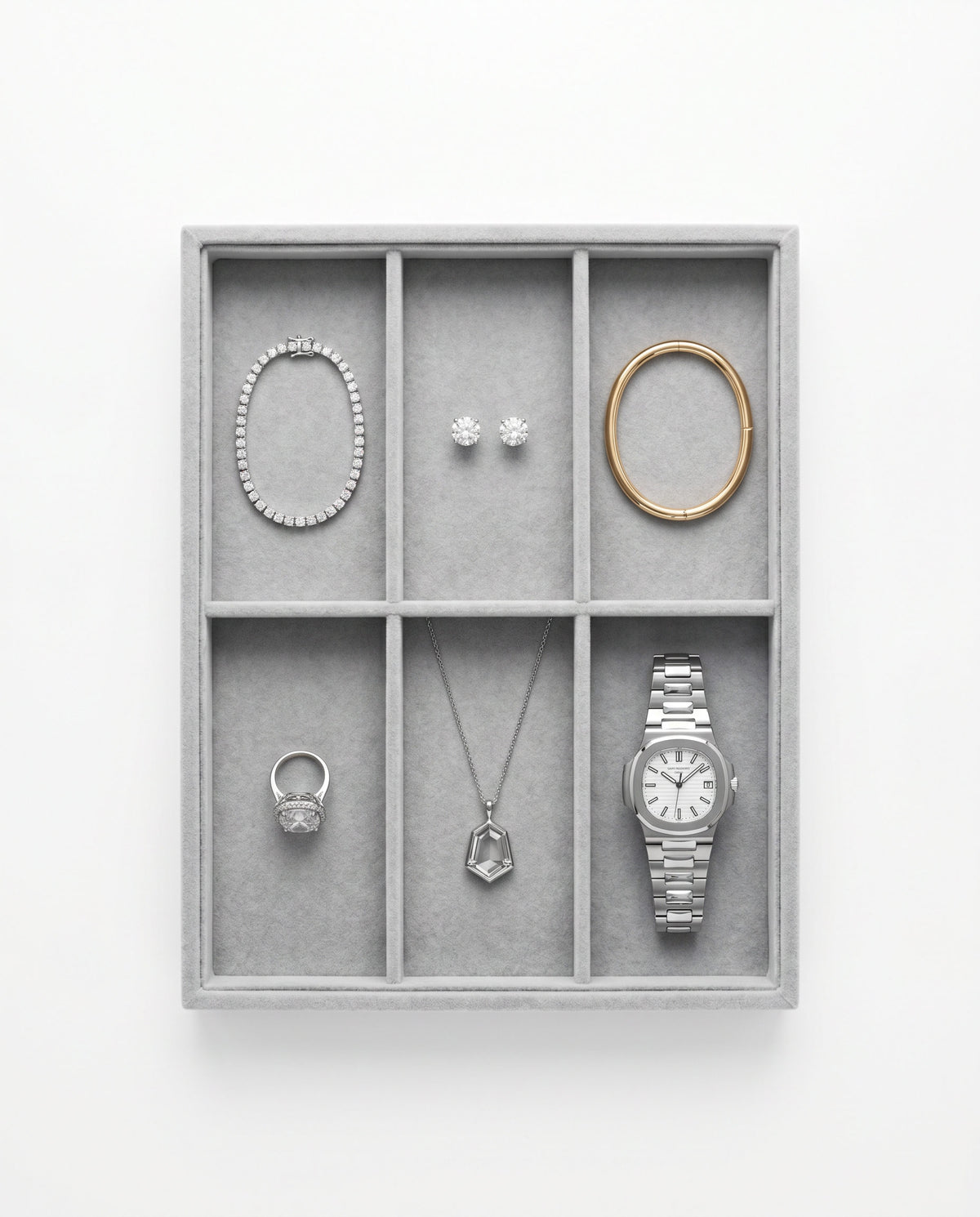 A six-compartment jewelry organizer tray in light gray velvet, styled with silver and gold jewelry including a bracelet, earrings, rings, necklace, and a watch, set against a plain white background.